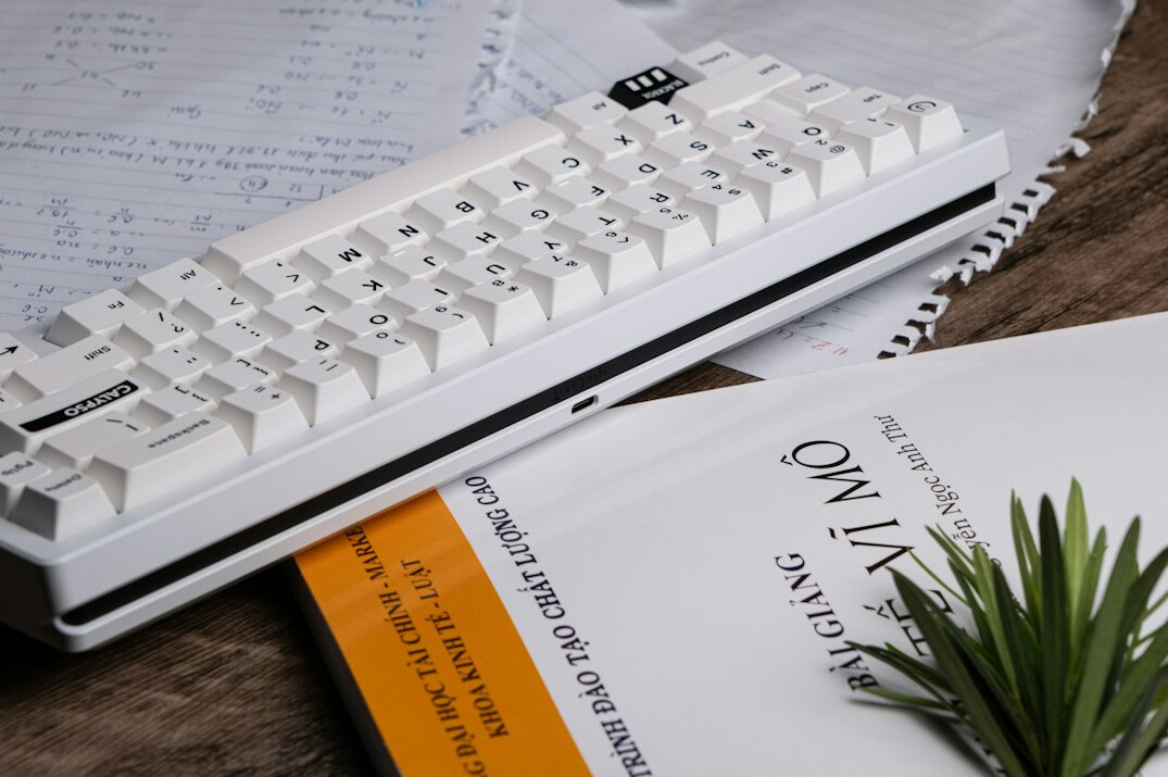 Stack of notebooks and a pen next to a mechanical keyboard